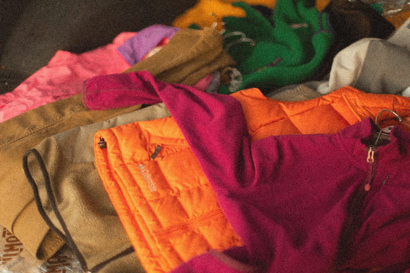A pile of puffy jackets in orange, magenta and green